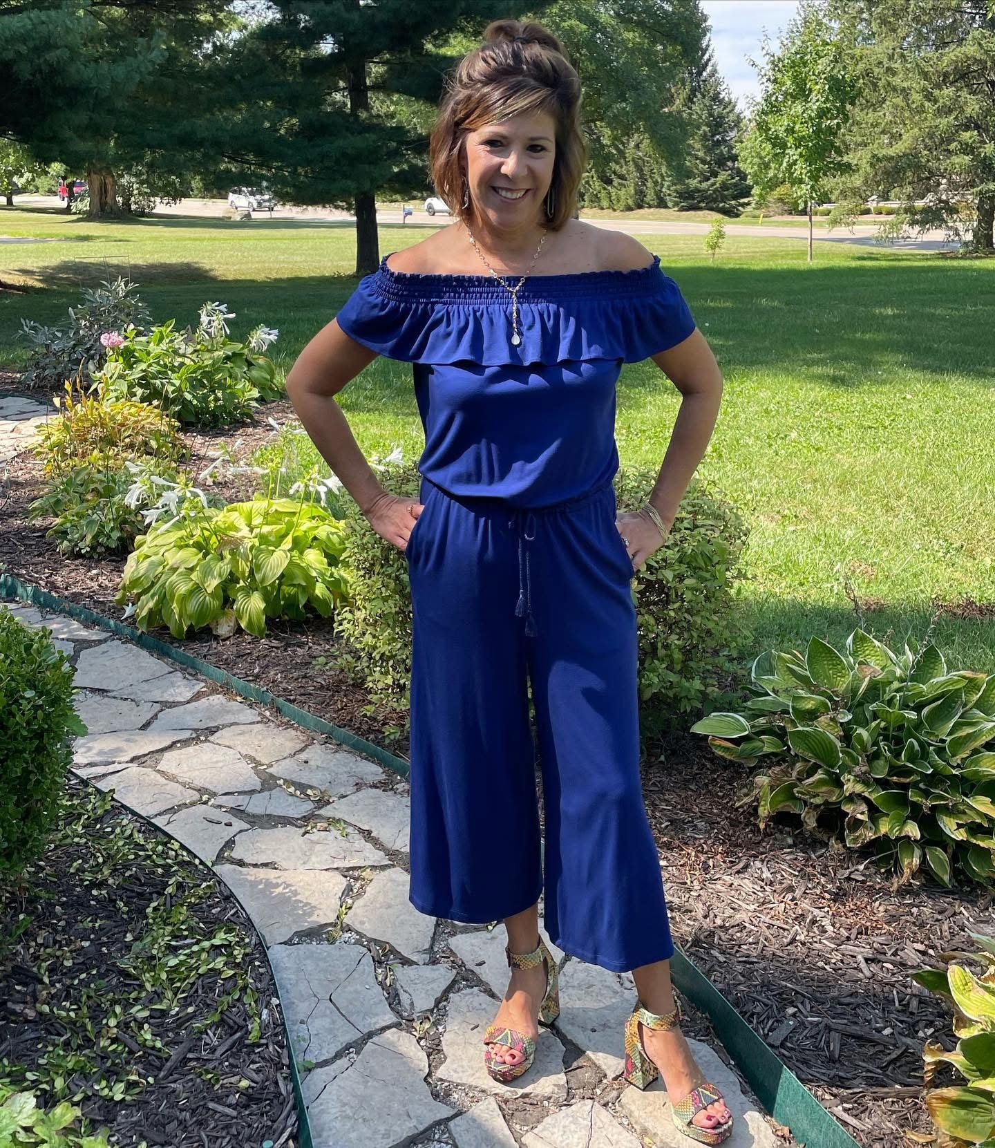 Woman modeling a blue off-shoulder jumpsuit in a garden setting from Twice Blessed boutique