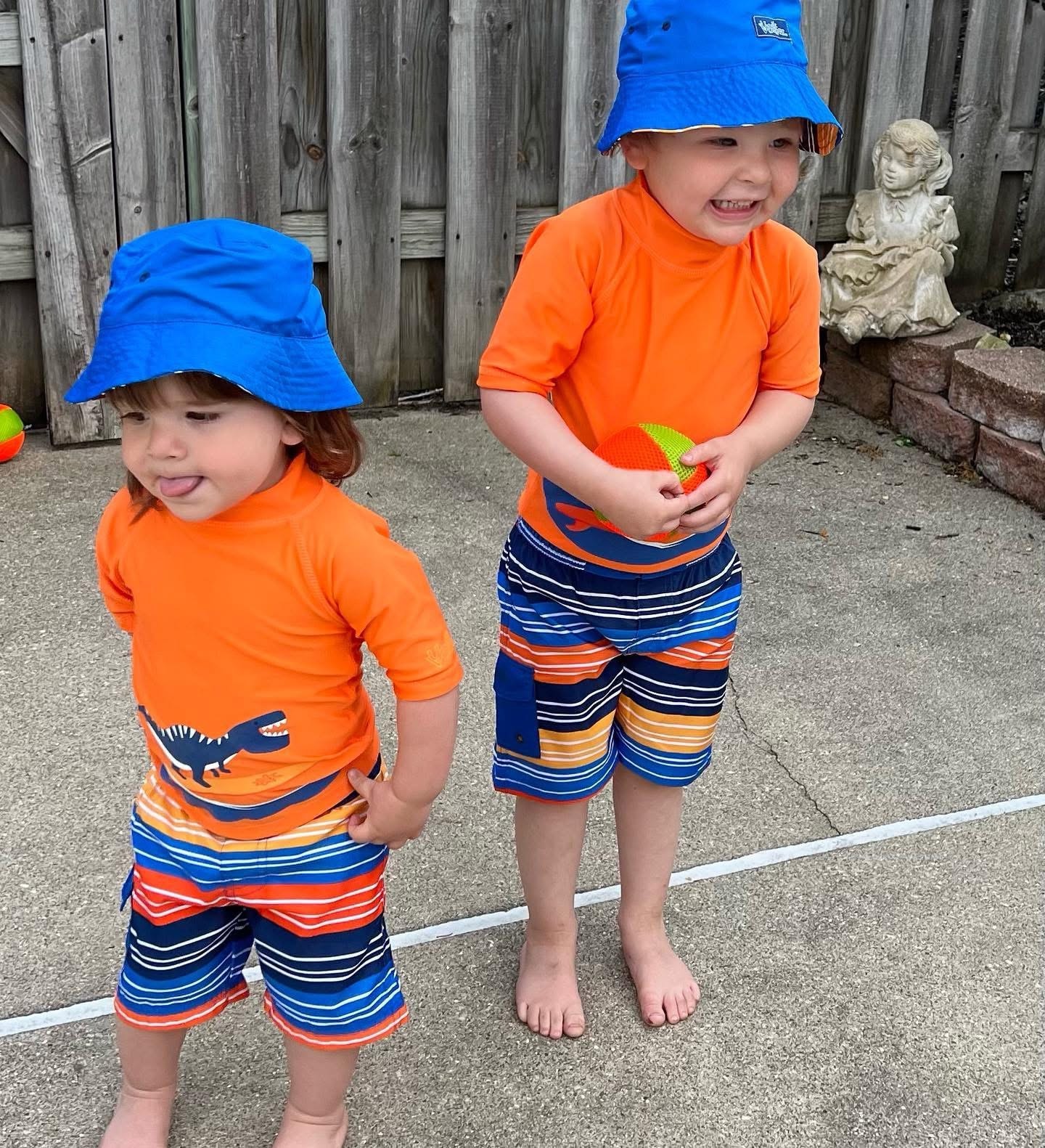 Two little boys in matching orange swim shirts and blue bucket hats