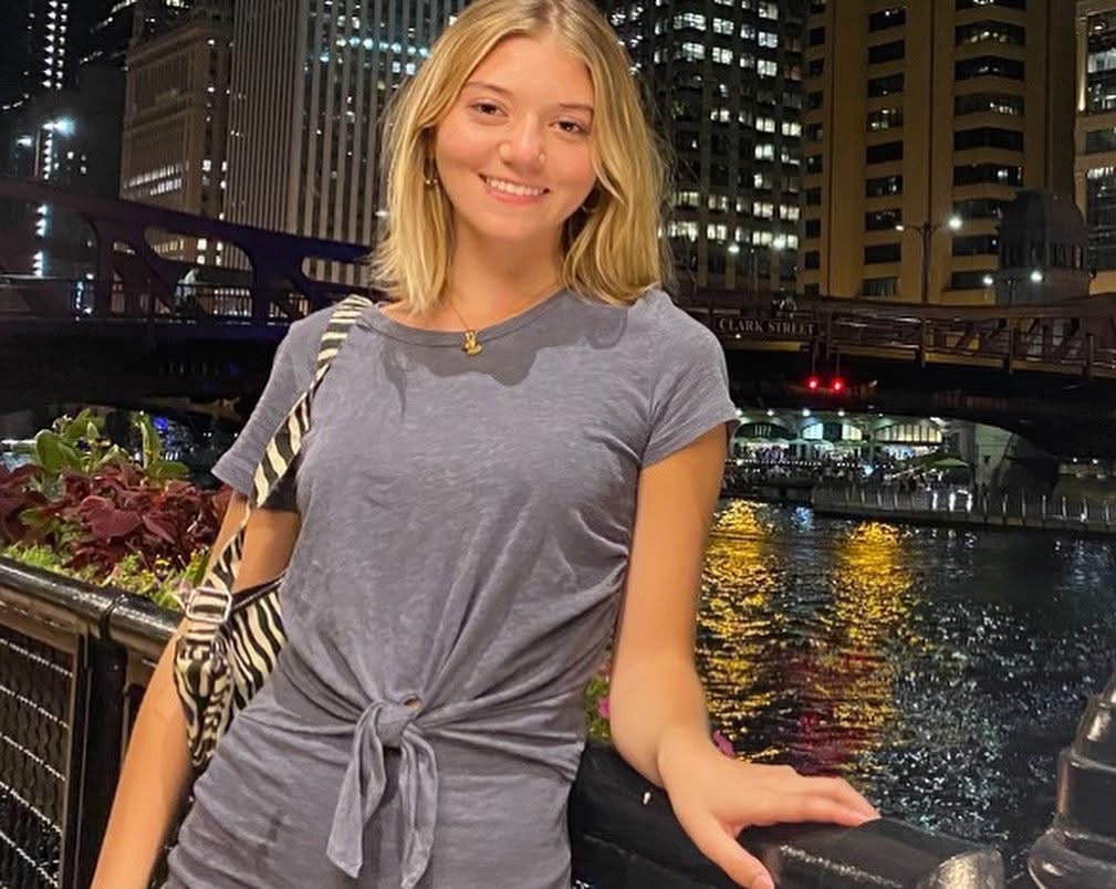 Young woman wearing a gray tie-front top with a zebra print bag by the Chicago River at night