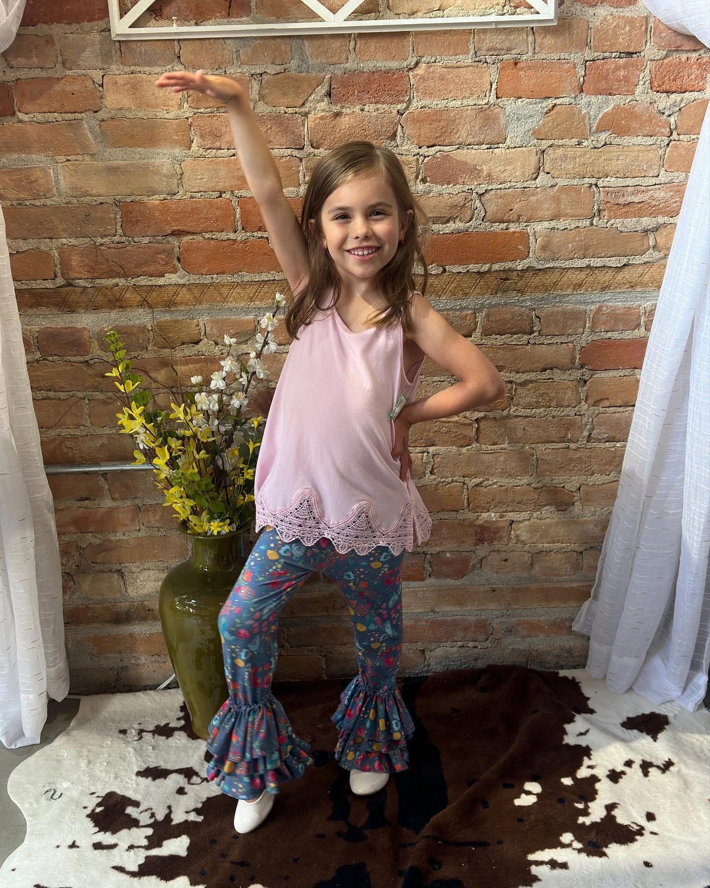Little girl in pink lace top and colorful flare pants dancing at Twice Blessed boutique