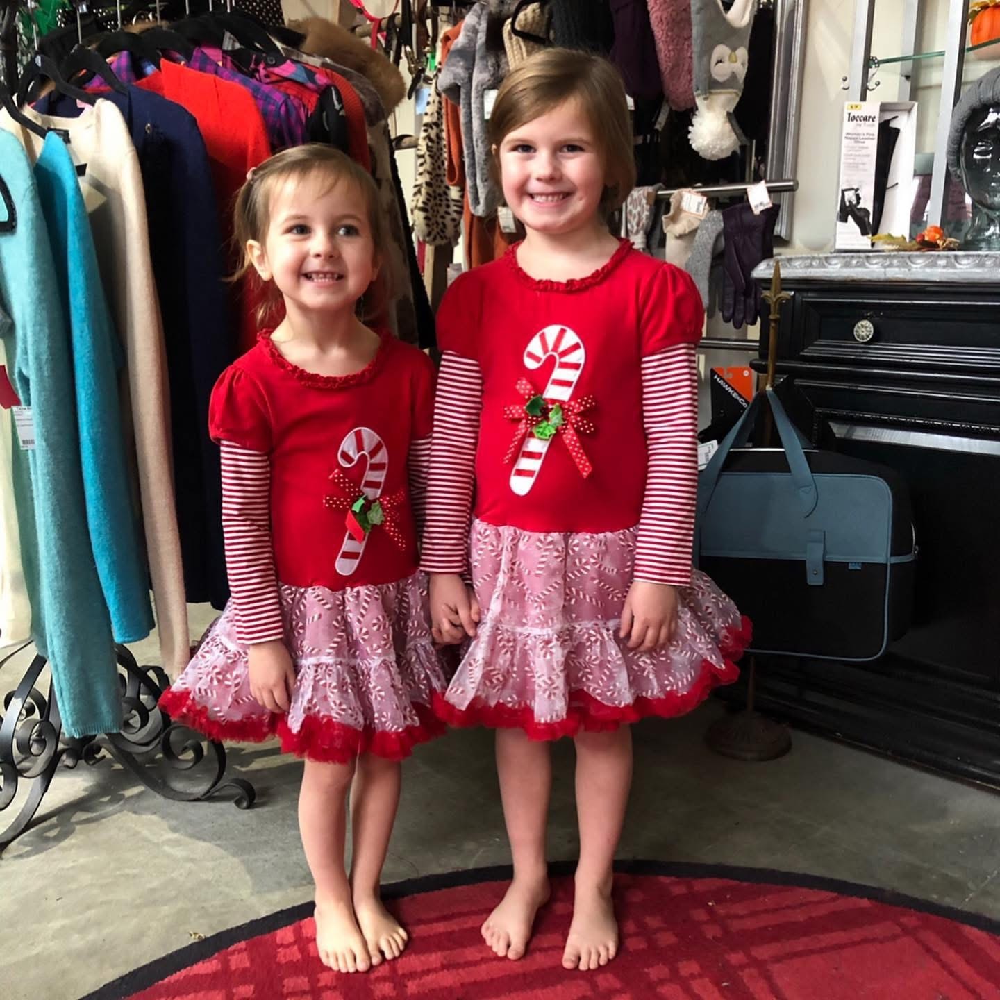 Two girls in matching red Christmas candy cane dresses at Twice Blessed boutique