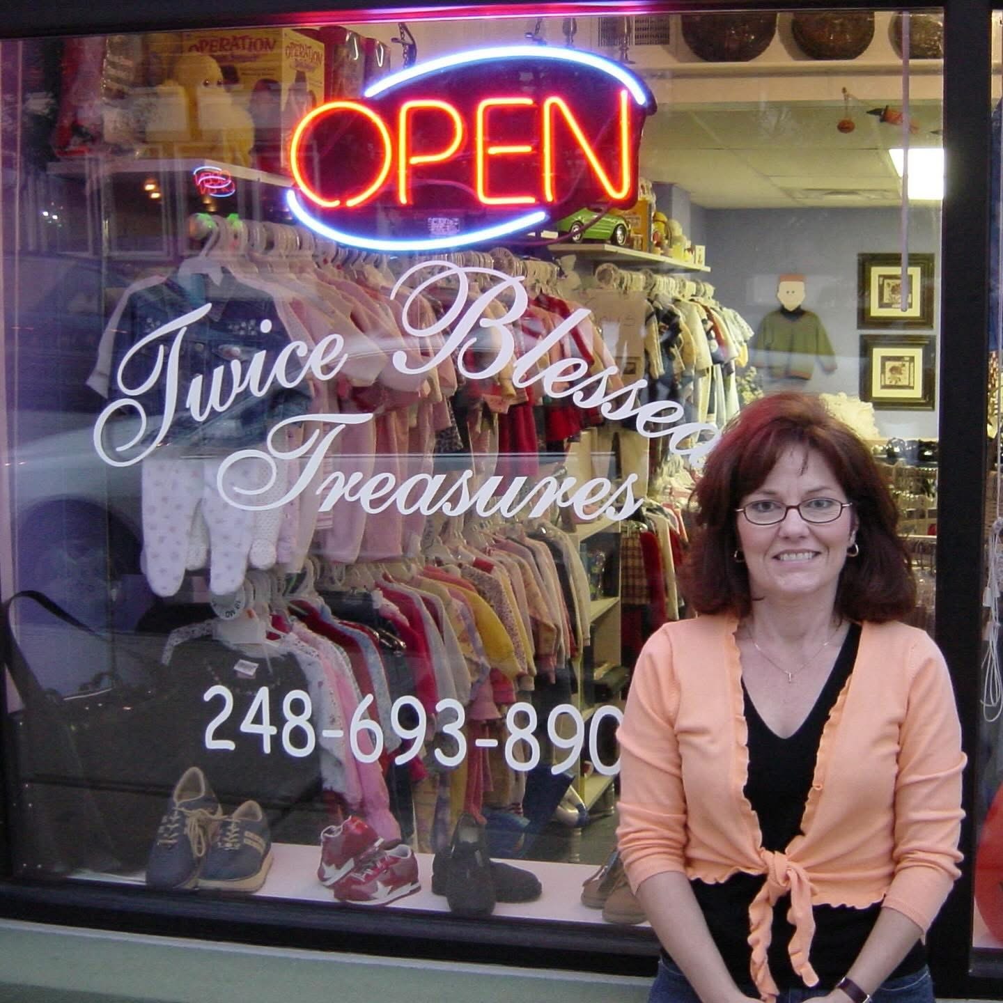 Owner smiling in front of the Twice Blessed Treasures storefront with neon open sign