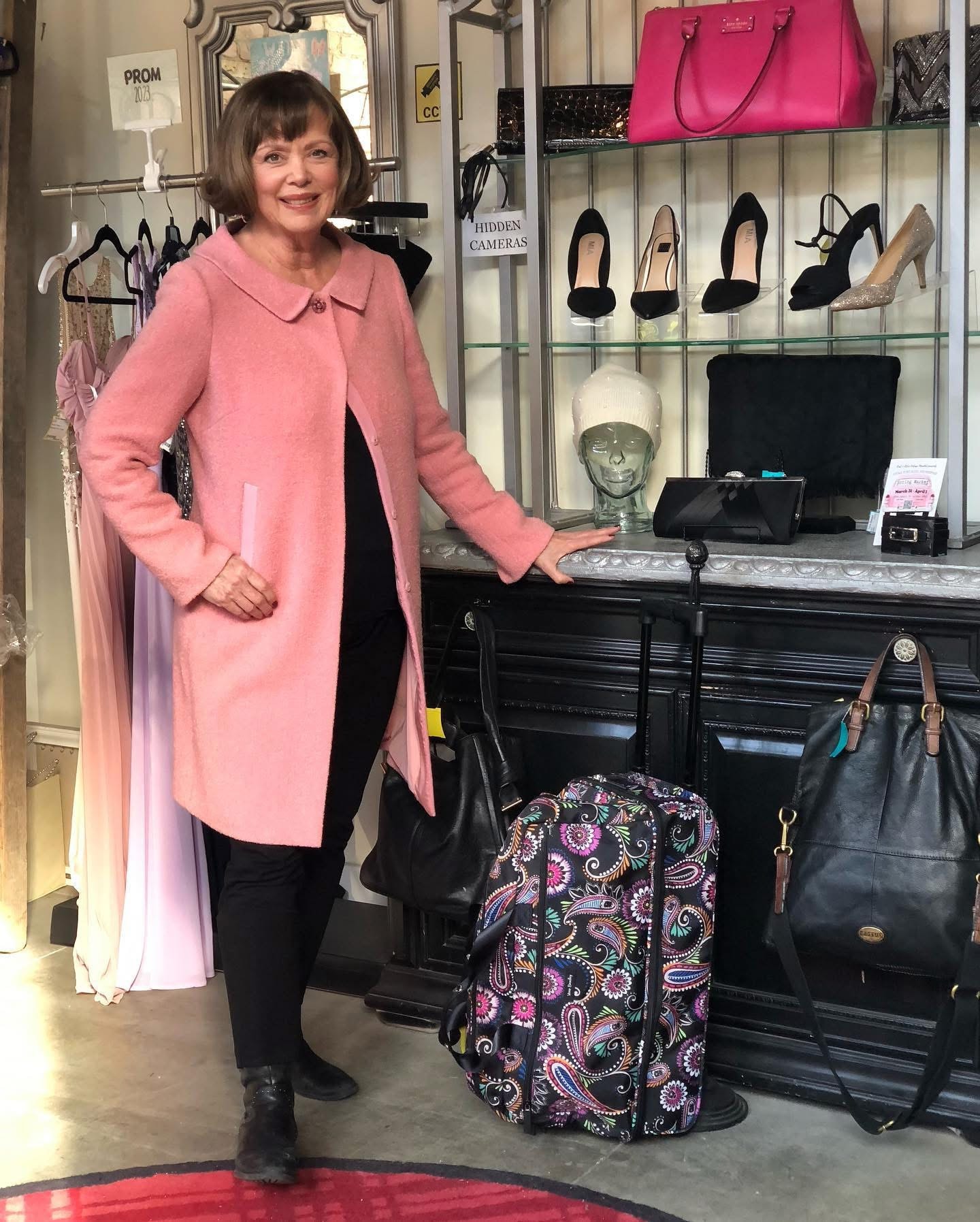 Elegant woman in pink coat with paisley luggage at Twice Blessed boutique