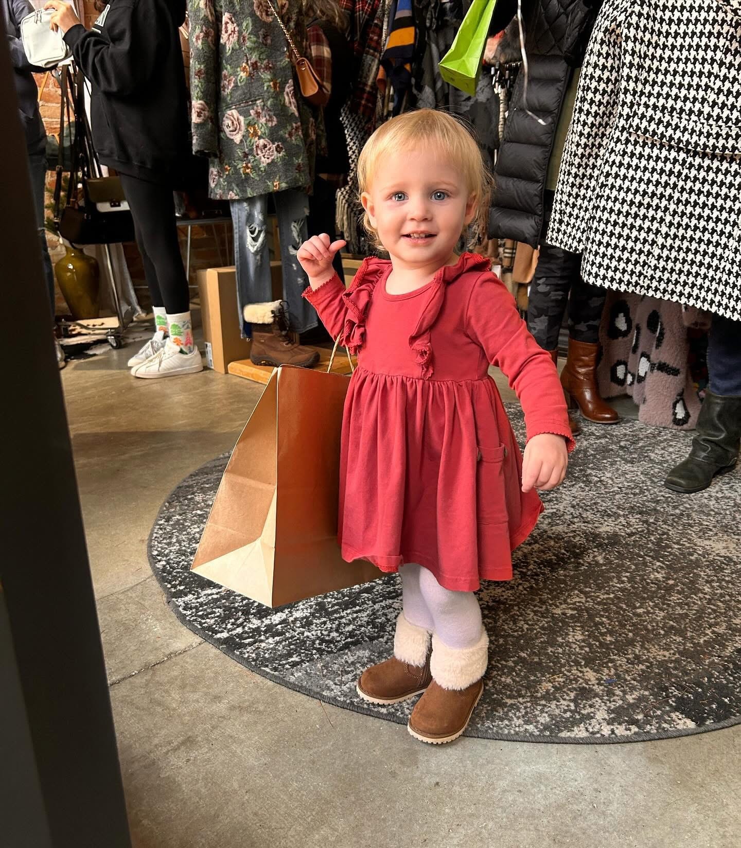 Adorable toddler in red ruffle dress holding a shopping bag at Twice Blessed boutique