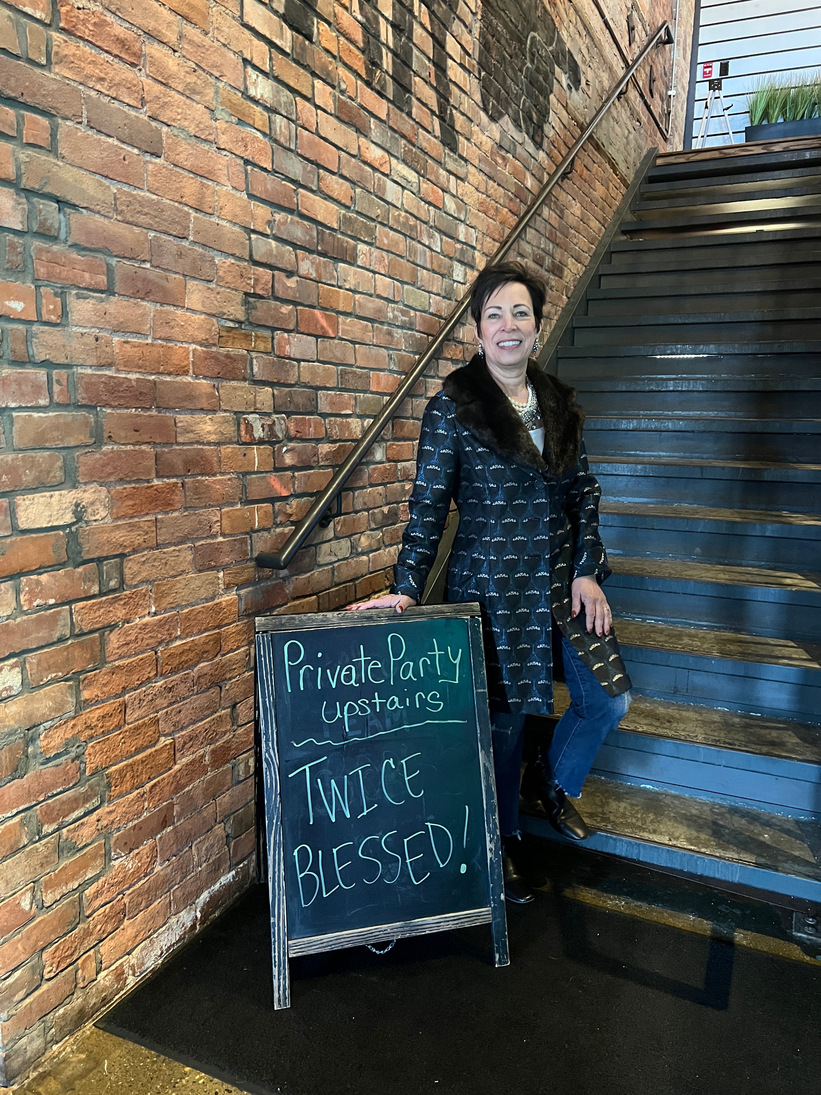 New owner posing with the Twice Blessed chalkboard sign at the Re-Grand Opening party
